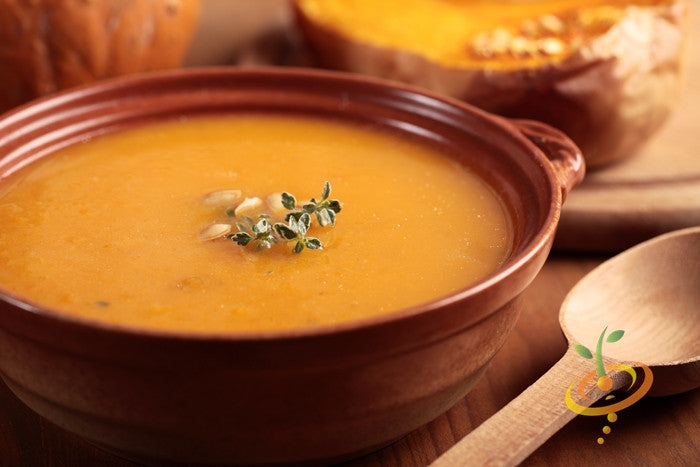 Creamy winter squash soup in a brown bowl garnished with herbs, with sliced butternut squash in the background